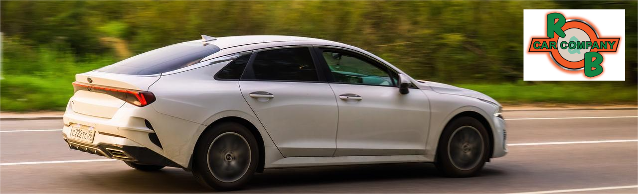 Kia K5 GT-Line sedan driving on a city road, showcasing its sporty design, sleek body lines, and modern exterior styling.