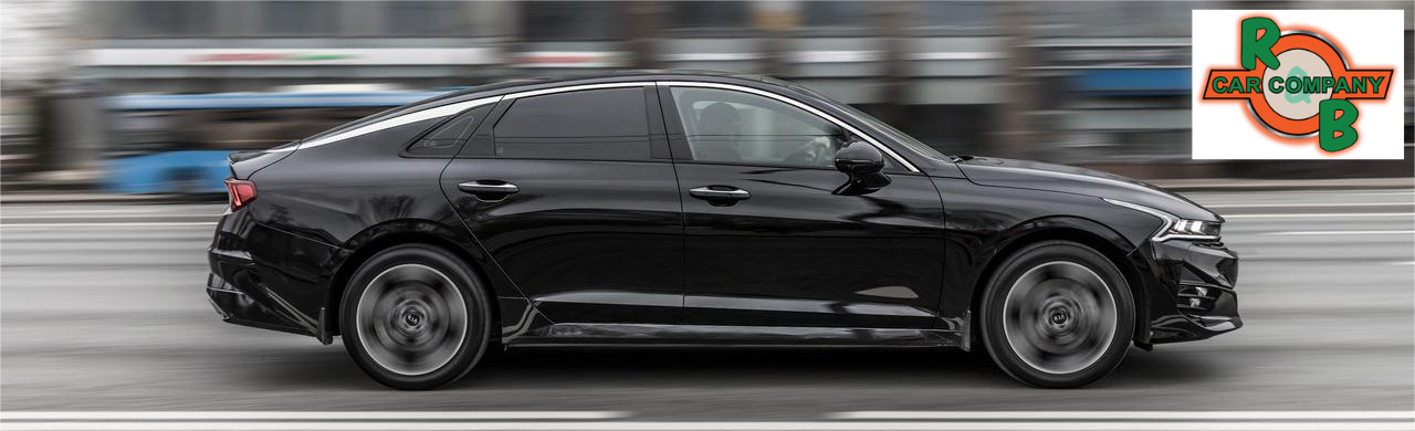 Sporty Kia K5 GT-Line sedan cruising through an urban street, highlighting its aggressive stance, smooth contours, and refined contemporary exterior design.
